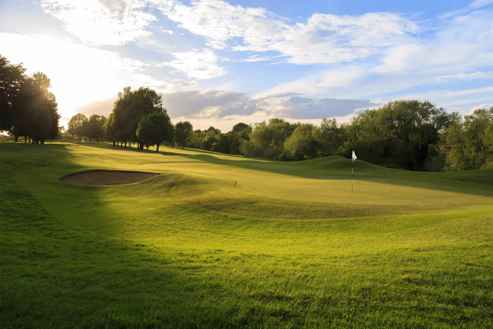 Sunlit golf course green with a flagstick and bunker